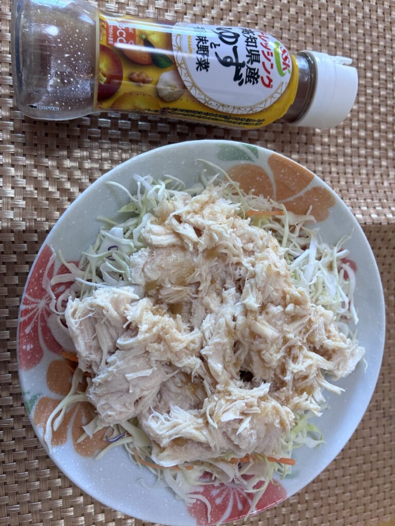 千切りキャベツの上にほぐしたミート21のサラダチキンを乗せてドレッシングをかけた皿と、ゆずと香味野菜のドレッシングの瓶を撮影した写真